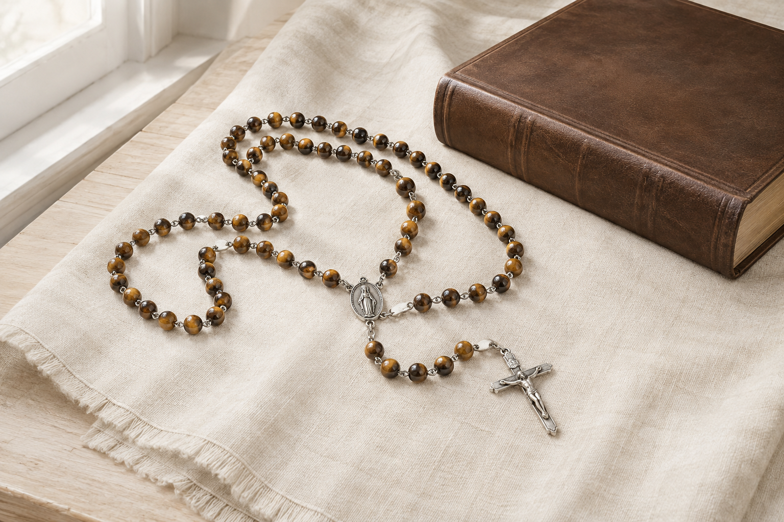 Chapelet catholique en œil de tigre avec crucifix près d’un livre de prière fermé