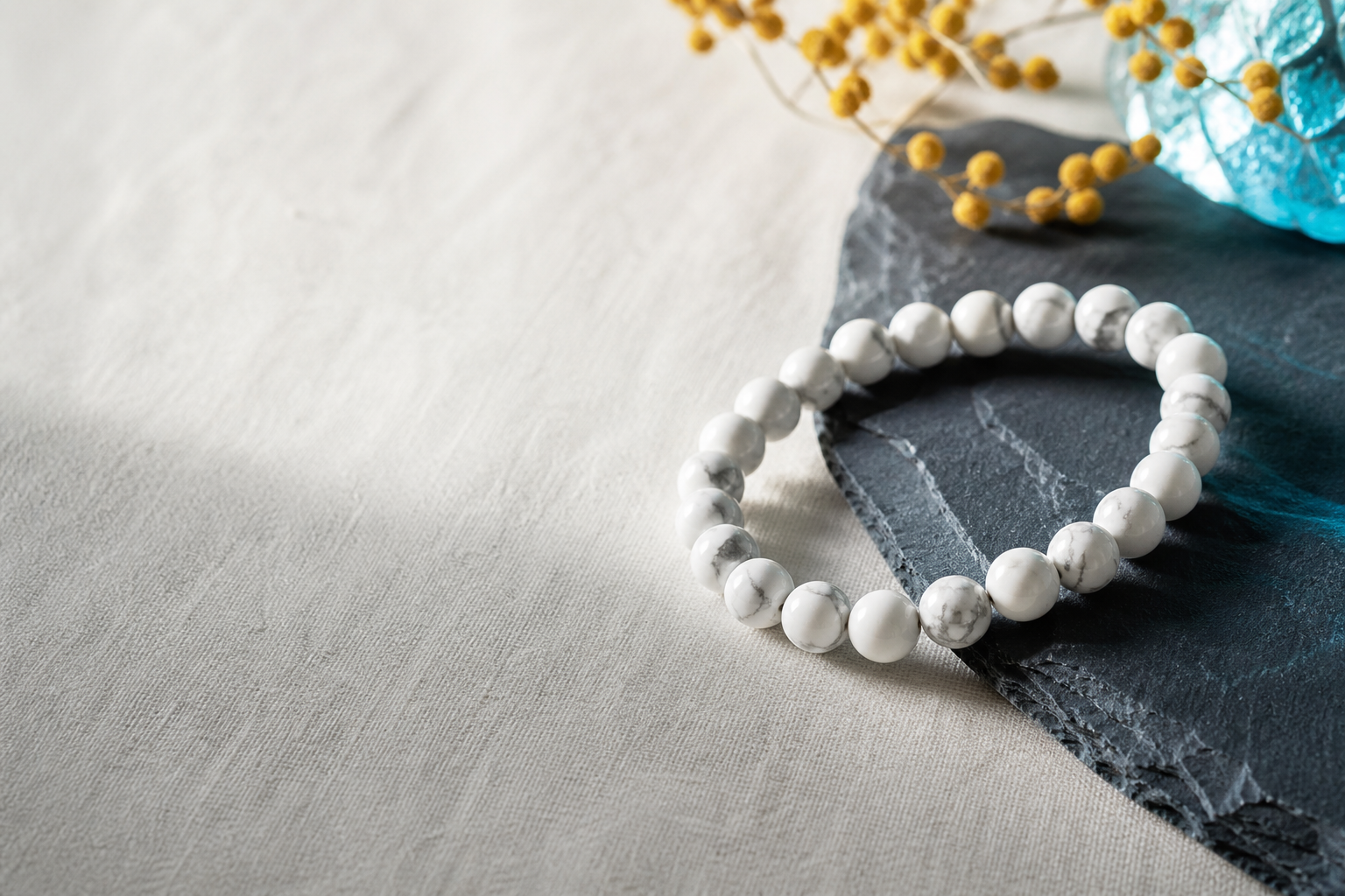 Bracelet en howlite blanche posé sur du lin et une ardoise bleu nuit