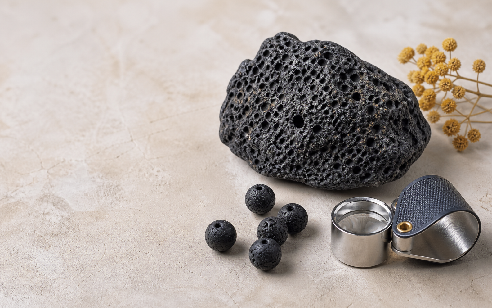 Pierre de lave noire brute, perles poreuses et loupe sur une table minérale